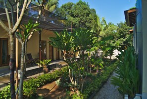 A garden with a pathway, potted plants, and a building with a sloped roof. - Ari La Casa (Penida Island)