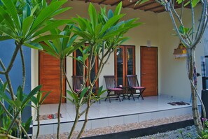 A covered outdoor seating area with chairs and a table, surrounded by lush greenery.