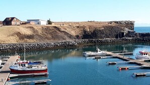 A marina with boats docked, a rocky shoreline, and a building in the background. - Hotel Duus (Reykjanesbær)