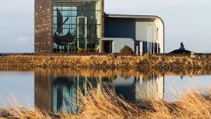 A modern building with a glass facade and a reflective water body in front. - Hotel Duus (Reykjanesbær)