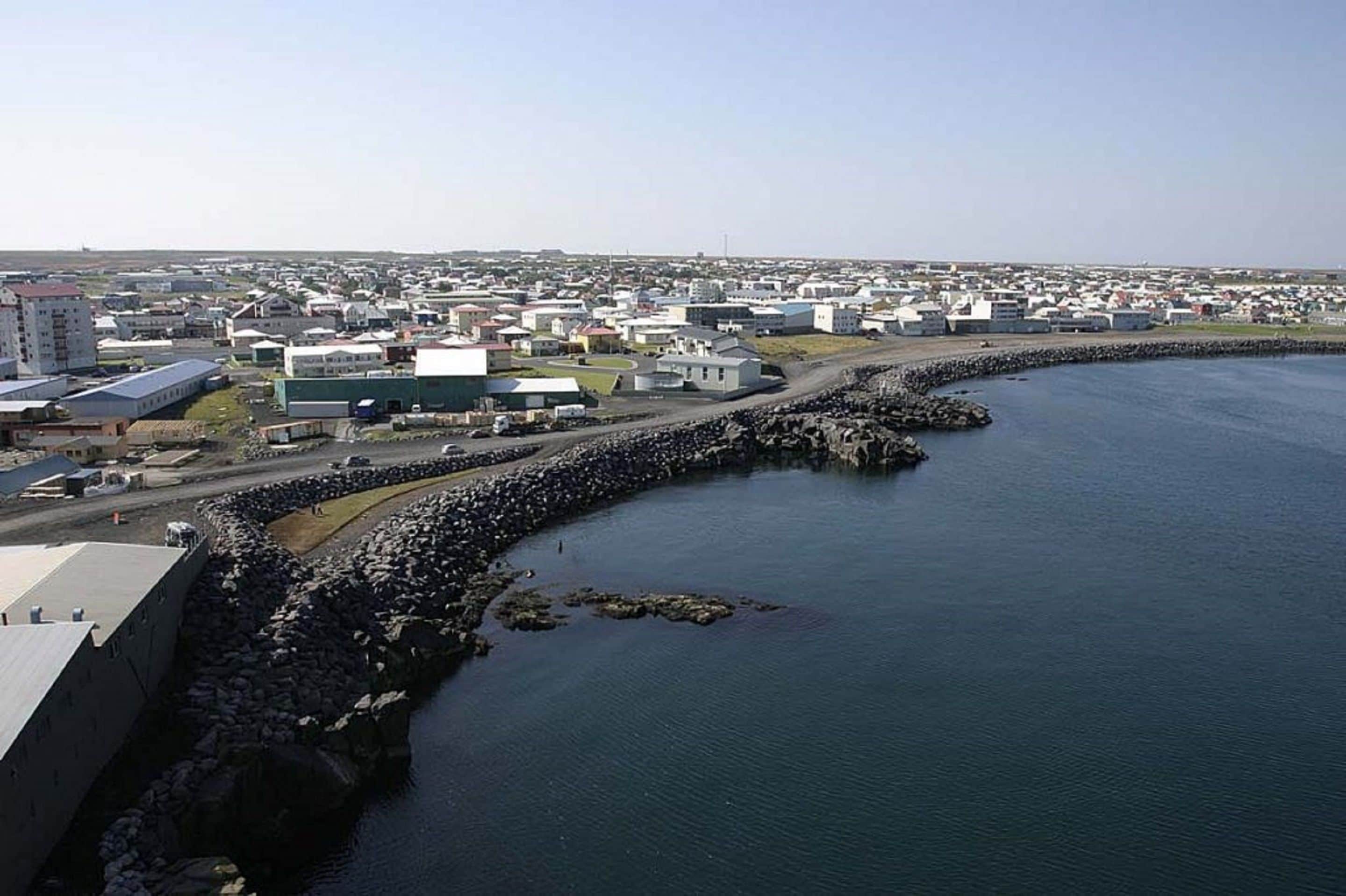 An aerial view of a coastal town with a prominent breakwater and industrial buildings along the waterfront.