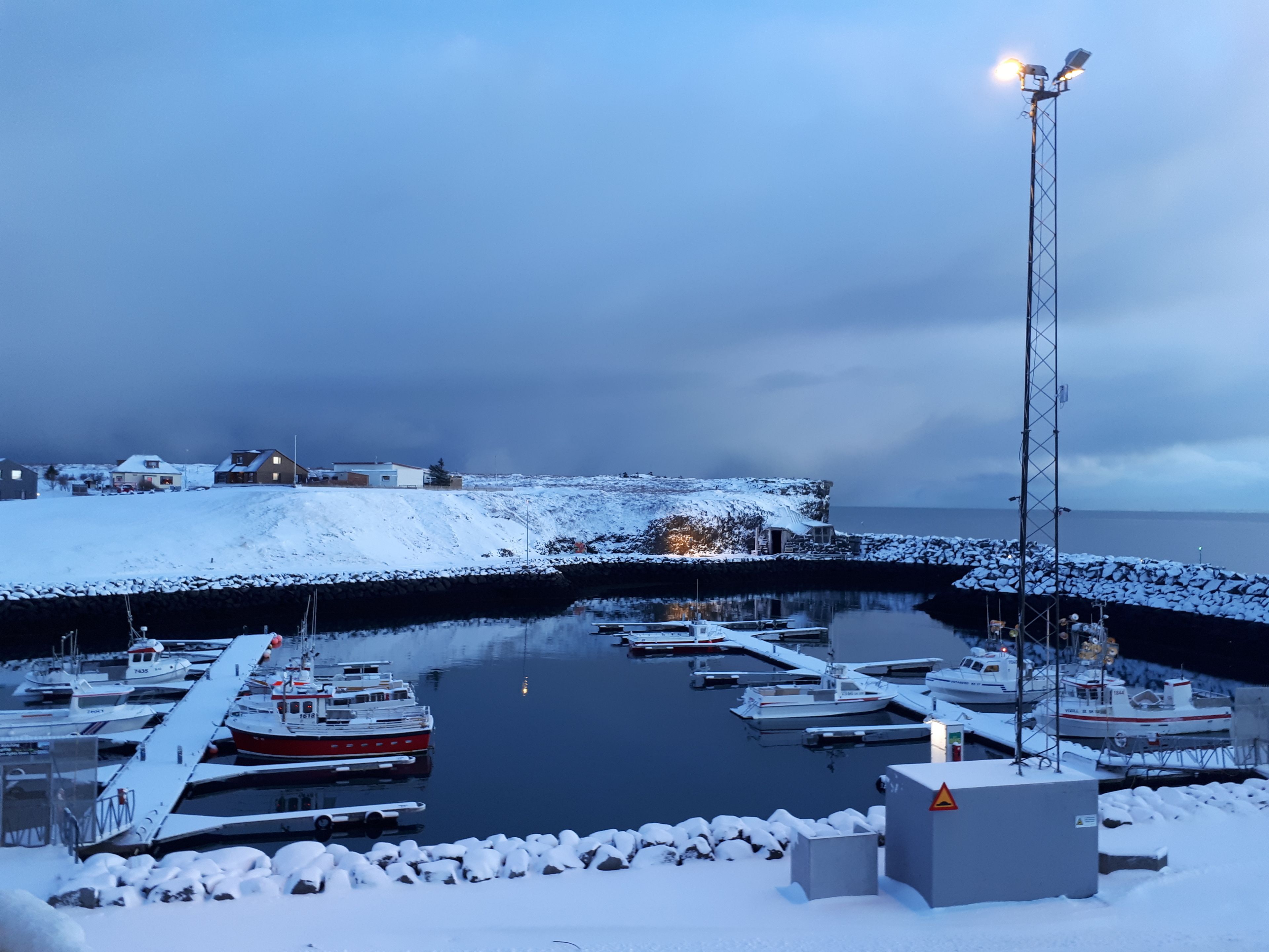 Un puerto deportivo con barcos amarrados, un faro y un paisaje nevado.