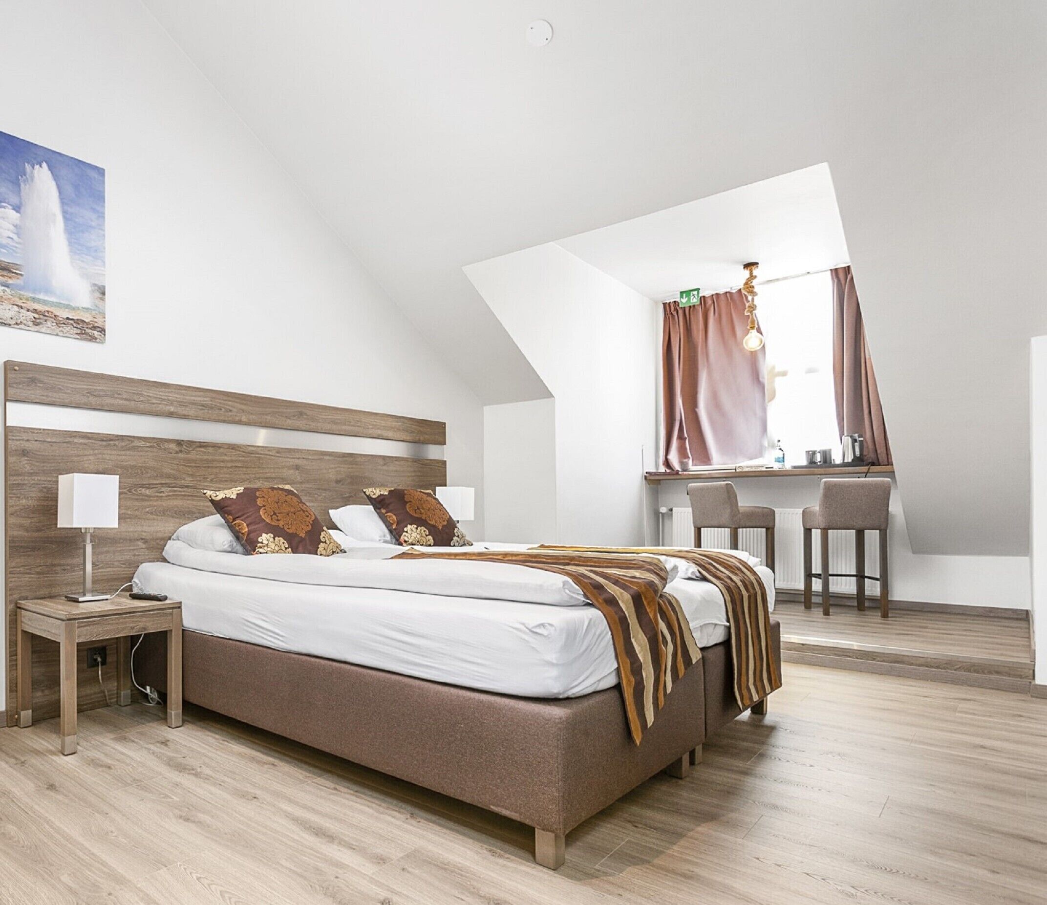 A modern bedroom with a large bed, a desk, and a view of the outdoors.