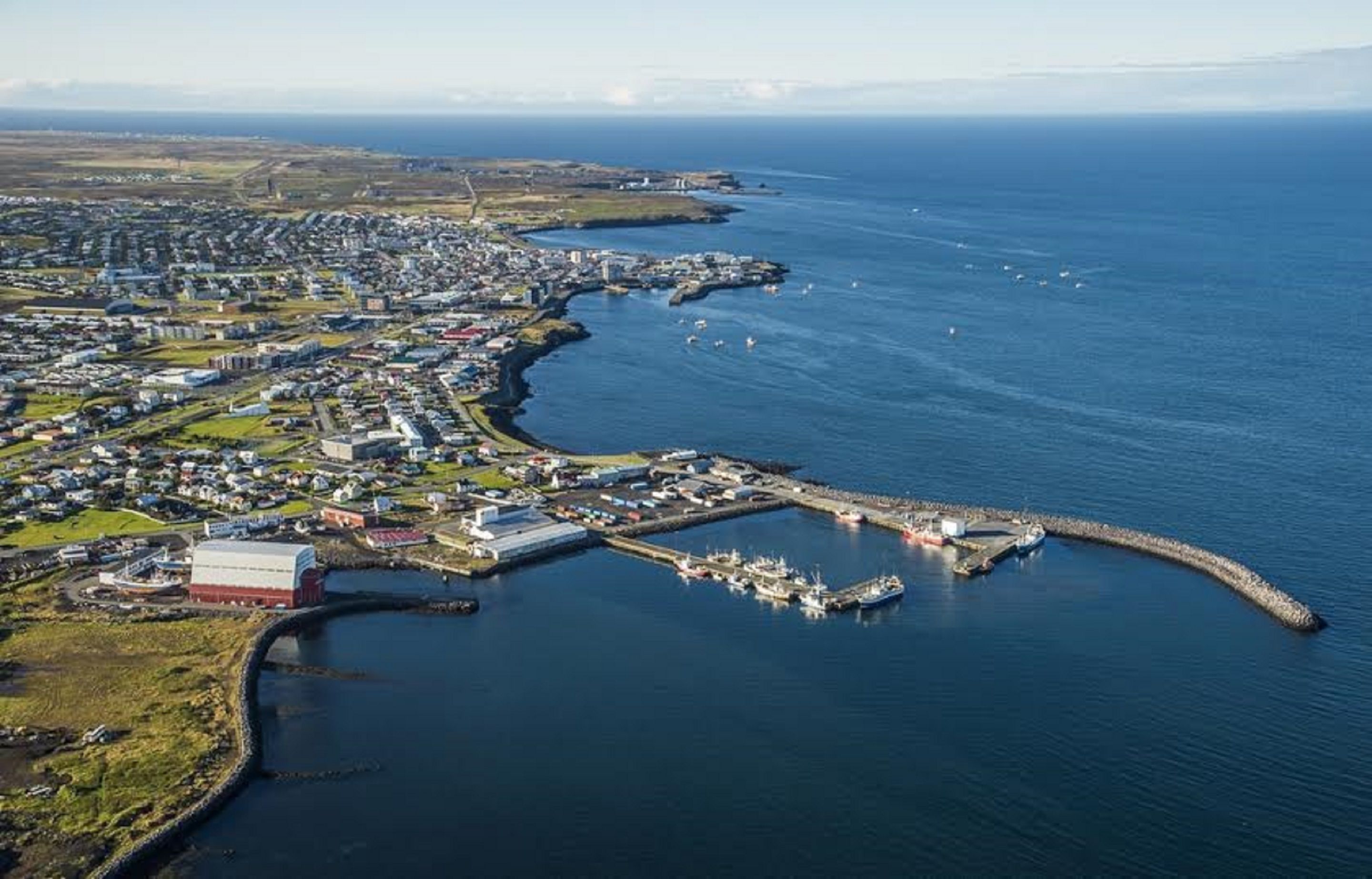 An aerial view of a coastal town with a marina, residential areas, and a large industrial building.