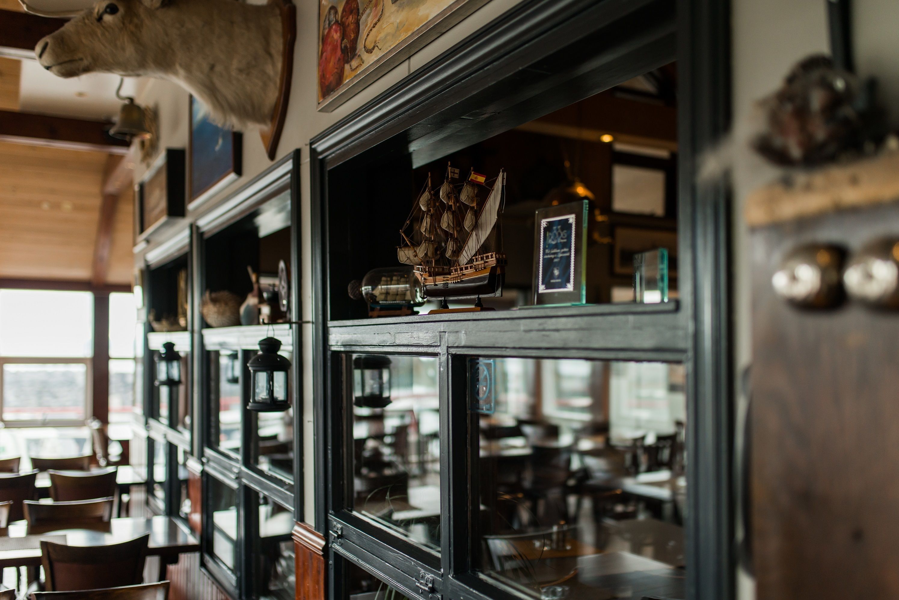A restaurant interior with wooden furniture, a mounted cow head, and a ship model on the wall.