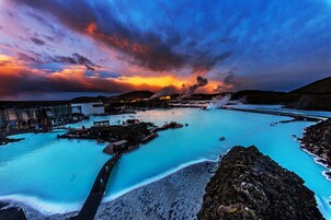 Un spa geotérmico con una piscina grande, un paseo de madera y montañas al fondo.