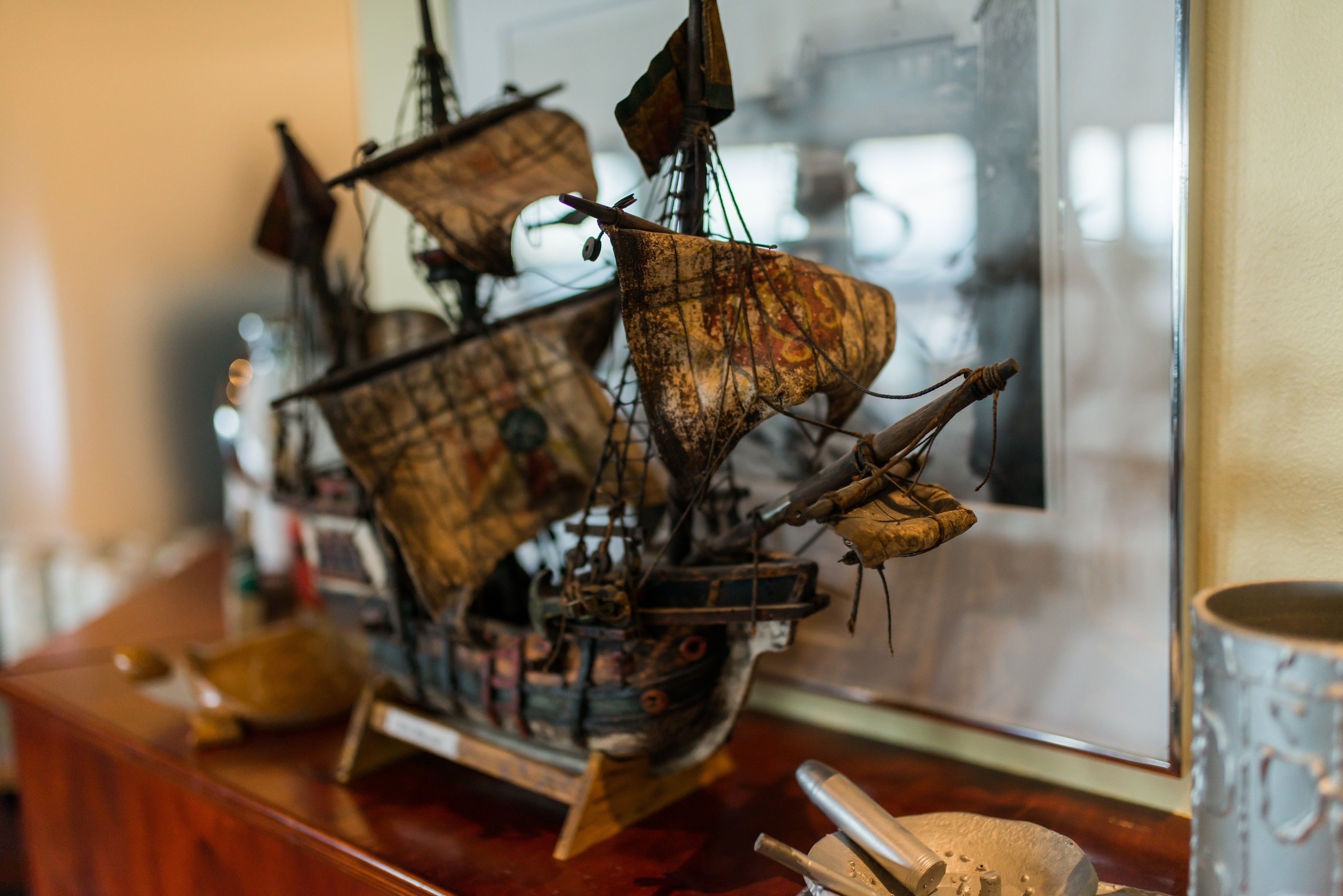 Une maquette de bateau est posée sur une surface en bois, et un tableau encadré se trouve à l’arrière-plan.