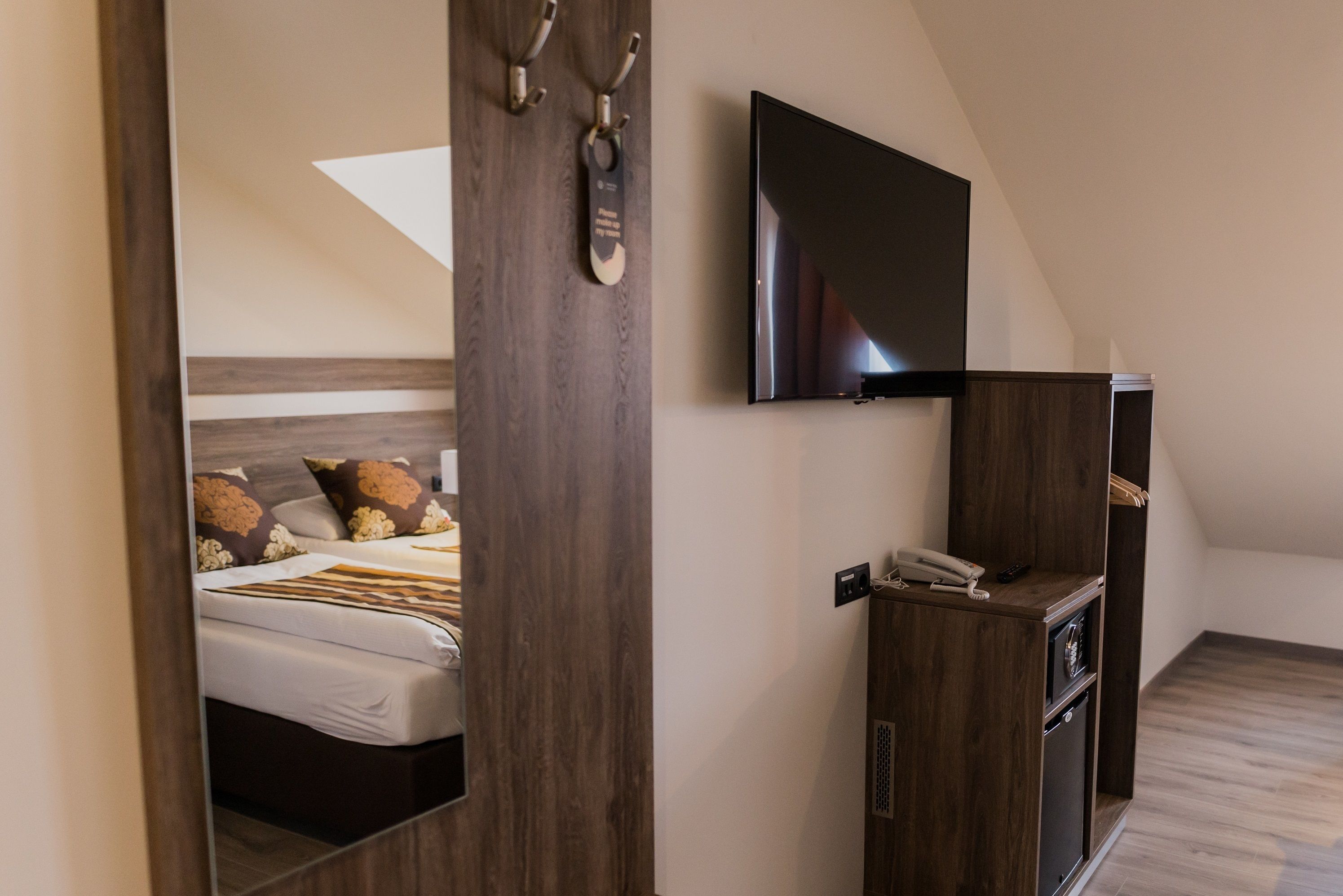 Un dormitorio con cama, televisor montado en la pared y un armario de madera con teléfono.