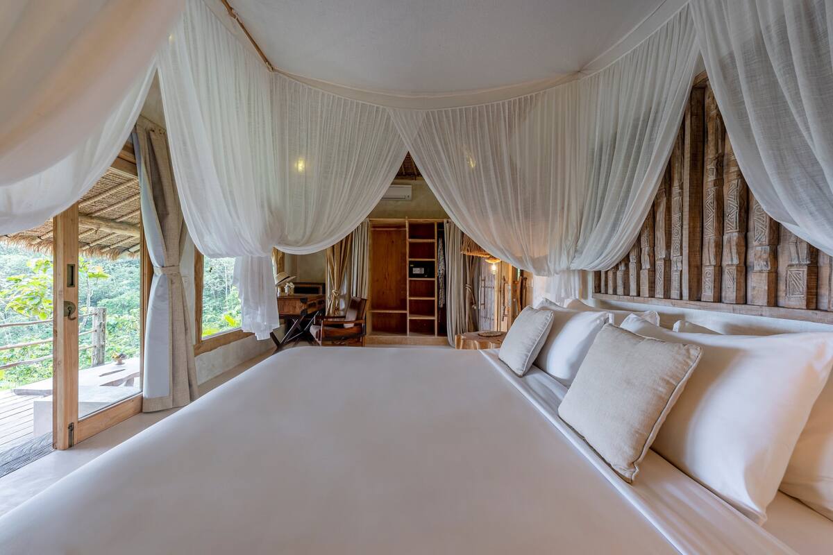 Une chambre spacieuse avec un grand lit, des rideaux blancs et une vue sur l’extérieur.