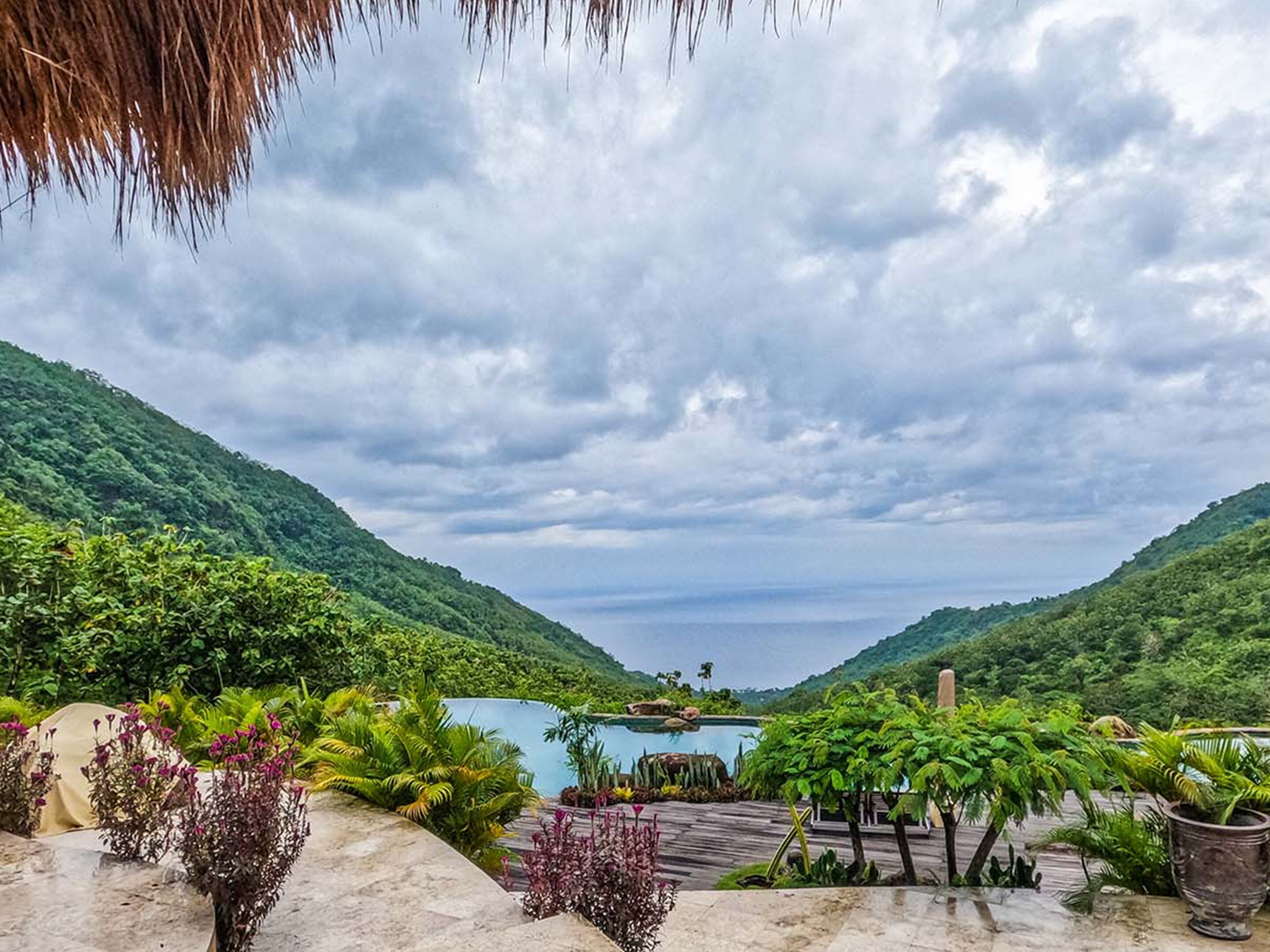 A tropical resort with a pool, lush greenery, and a mountainous backdrop.