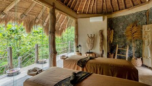 A room with two beds, a stone wall, and a thatched roof.