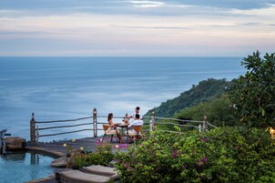 Terraza de madera con vistas a un cuerpo de agua, donde un grupo de personas cena.