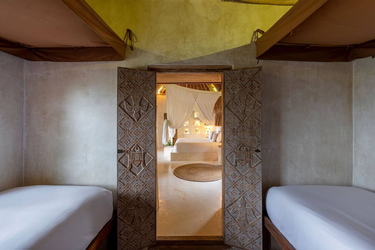 Une pièce avec deux lits, une porte décorée de motifs et une vue sur une chambre à coucher avec un lit et une lampe.