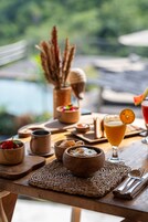 A wooden table with a woven placemat, a glass of orange juice garnished with an orange slice, wooden bowls, and a wooden cup.