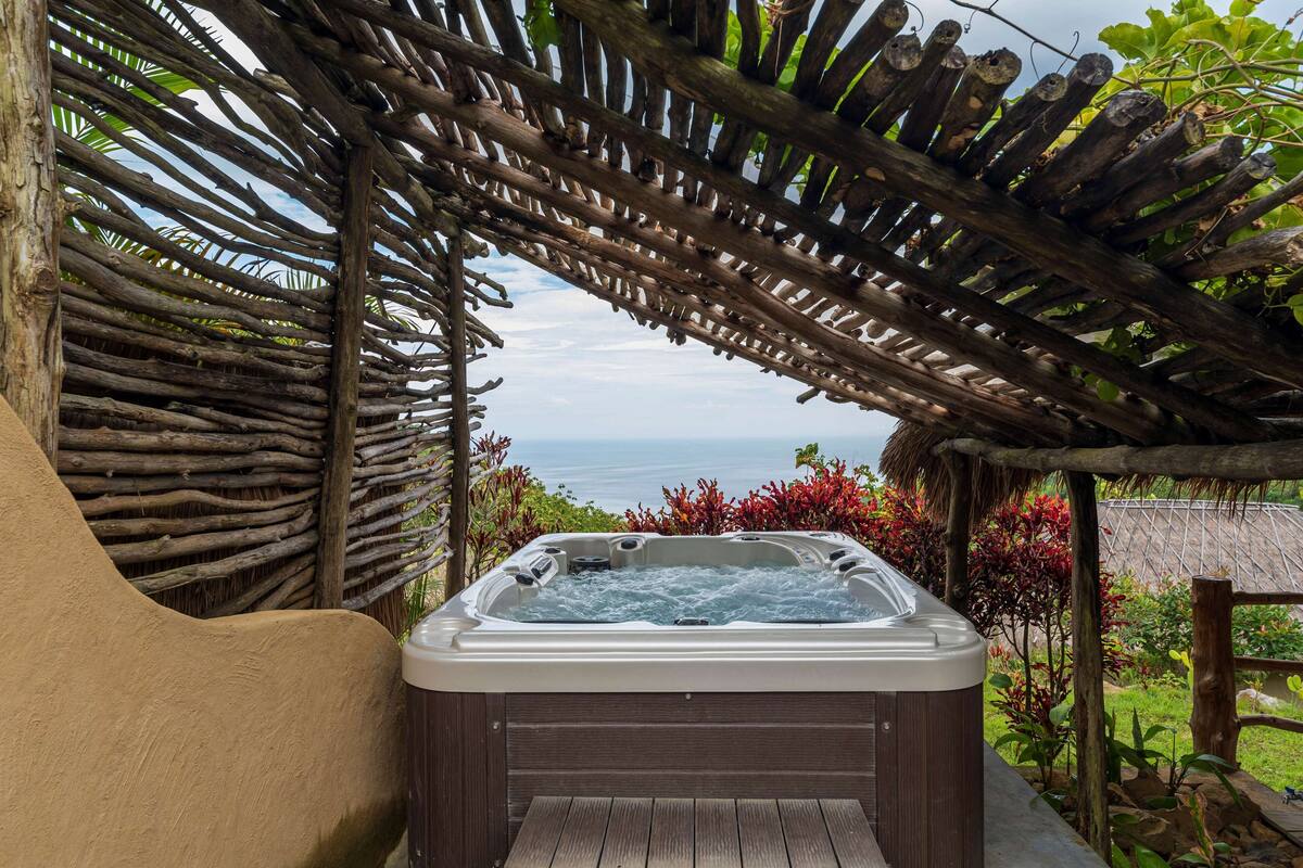 Un bain à remous sous une pergola en bois, avec vue sur l’océan.