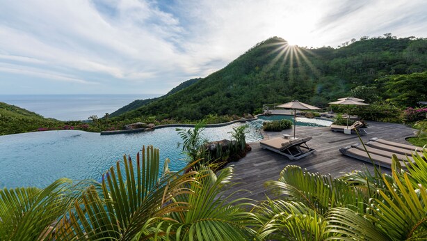 A resort pool area with a wooden deck, lounge chairs, and umbrellas.