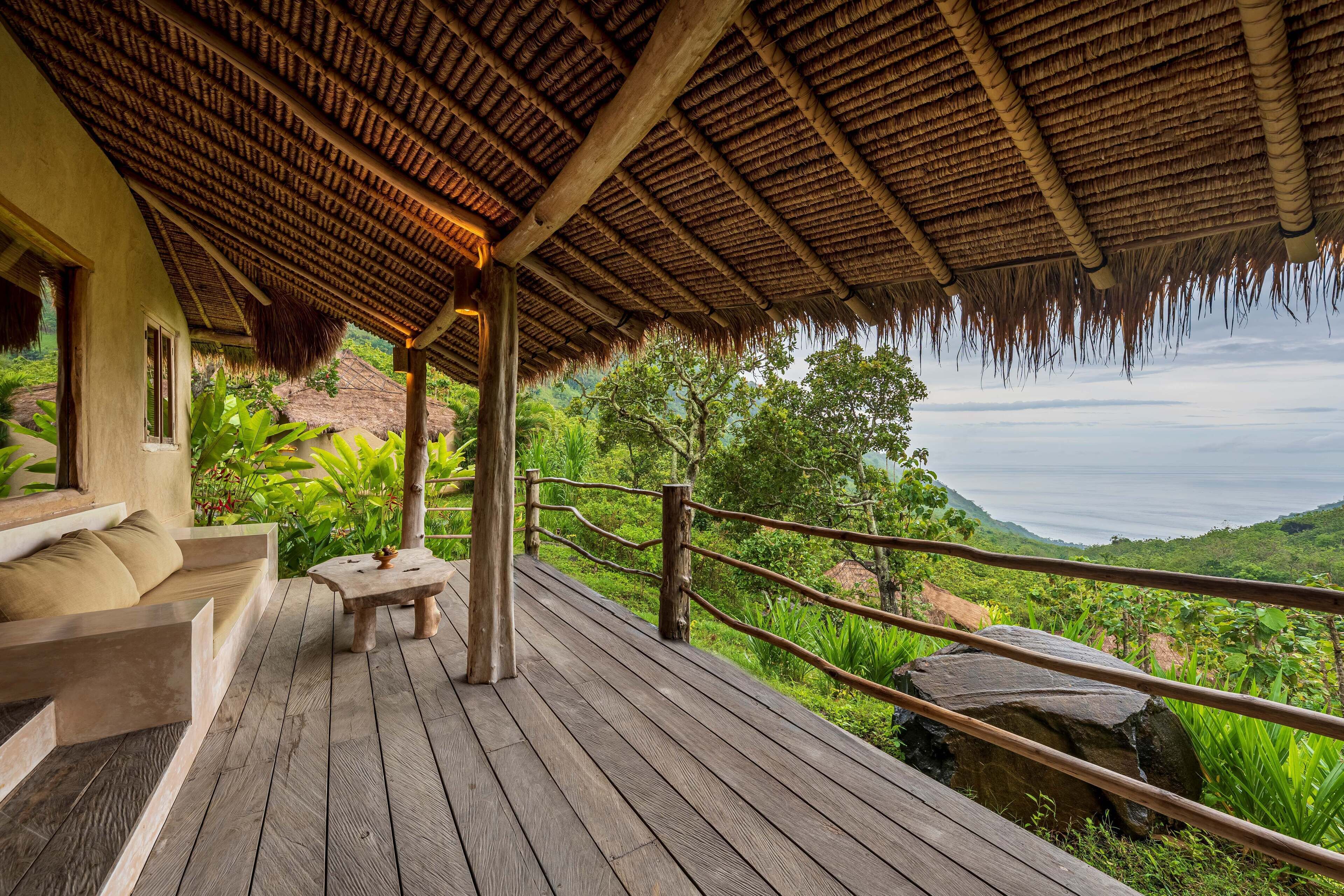 A wooden deck with a thatched roof, a sofa, and a table.