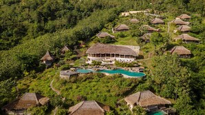 An aerial view of a resort with multiple thatched-roof cottages, a central pool, and lush greenery.