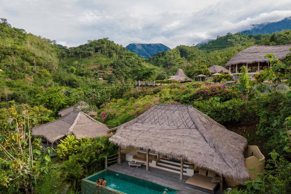 Un complexe hôtelier luxuriant de style tropical, doté d’une piscine, de bungalows aux toits de chaume et surplombant un paysage montagneux.