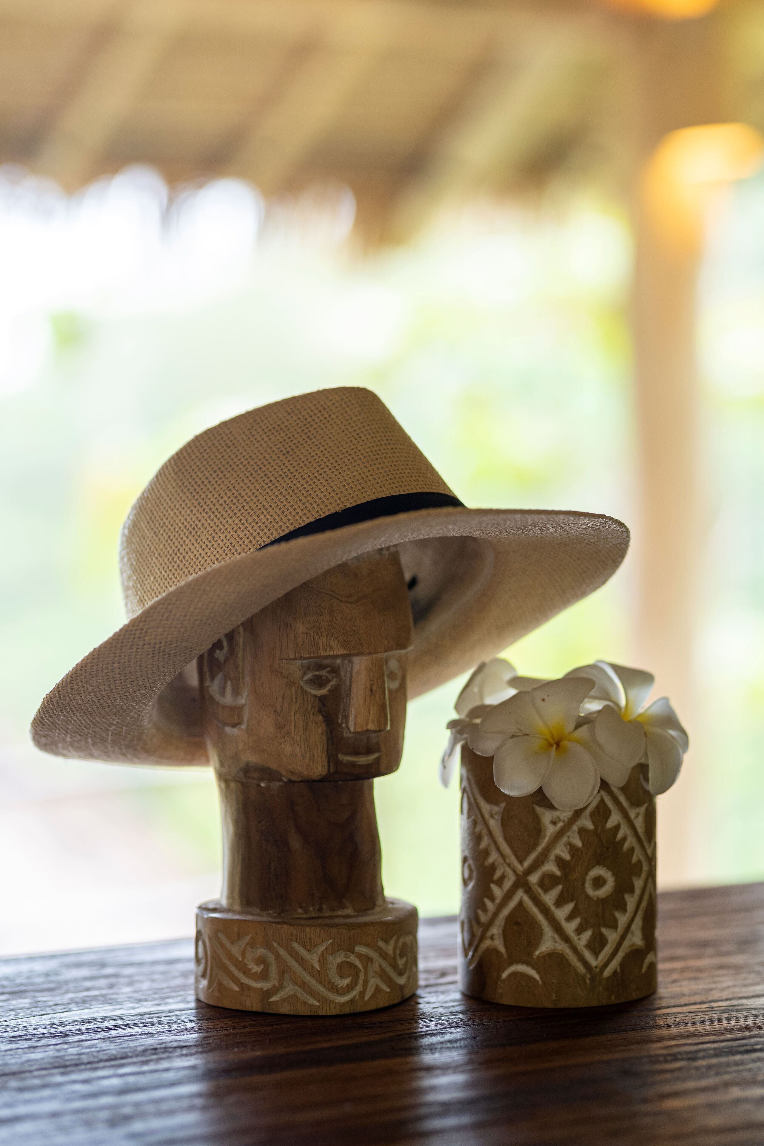 A wooden bust with a hat and a decorative vase with flowers.