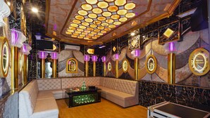 Une chambre luxueuse dotée d’un grand canapé d’angle, d’un petit coin bar et d’un plafond orné de luminaires hexagonaux.