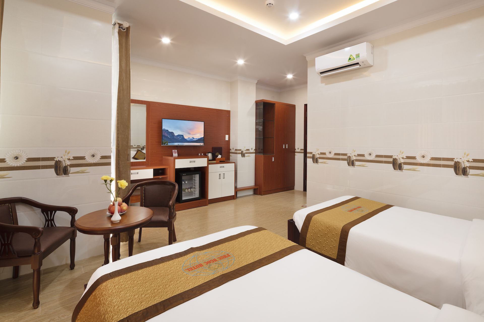 A hotel room with two beds, a desk, a chair, a television, and a minibar.