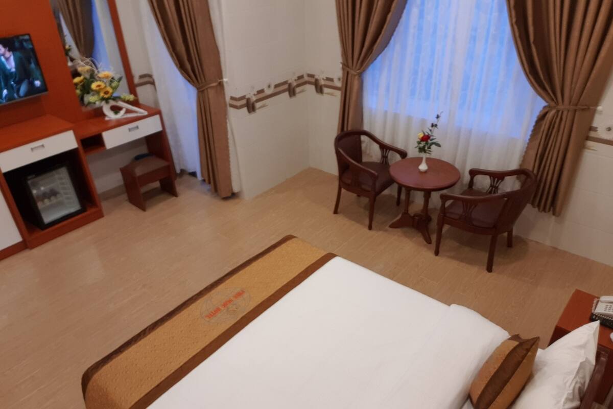 Habitación de hotel con cama, escritorio con televisor, pequeña mesa con sillas y cortinas.