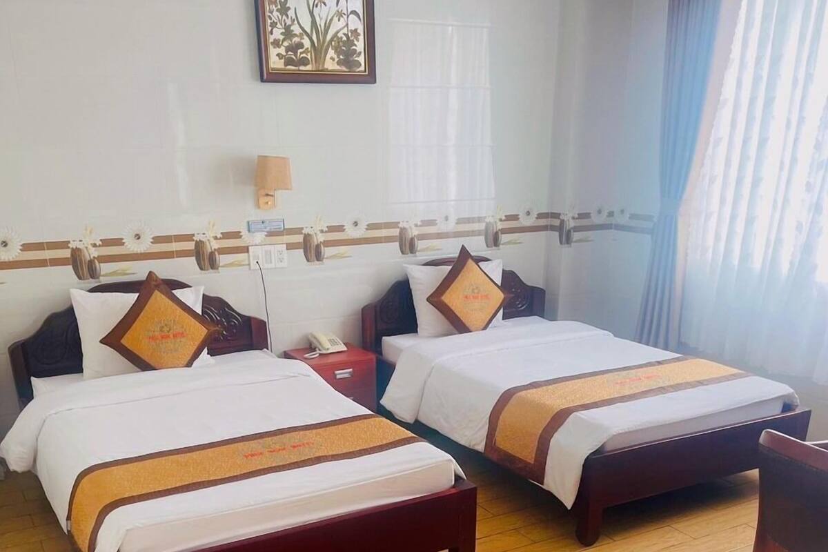 Habitación de hotel con dos camas, suelo de madera, una mesita de noche con teléfono y una obra de arte colgada en la pared.
