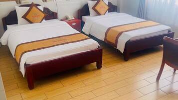 A hotel room with two beds, wooden flooring, a bedside table with a lamp, and a framed picture on the wall.