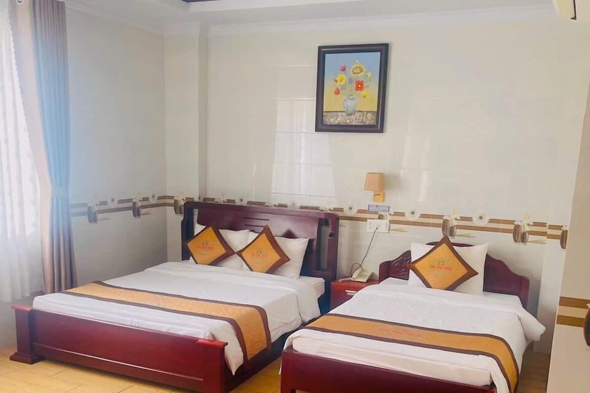 Habitación de hotel con dos camas de madera, suelo de madera, un cuadro en la pared y una ventana con cortinas.