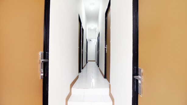 A long, narrow hallway with doors on both sides and a tiled floor. - Kamar Keluarga Bandara VII Syariah (Tangerang)