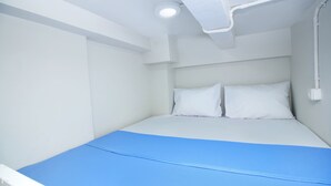 A small, single-bed room with white walls and a blue mattress. - Kamar Keluarga Bandara VII Syariah (Tangerang)