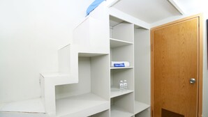 A white staircase leading to a wooden door, with a shelf containing two bottles and a box. - Kamar Keluarga Bandara VII Syariah (Tangerang)