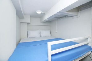 A single bed with a blue mattress and white headboard in a room with white walls and a ceiling light fixture.