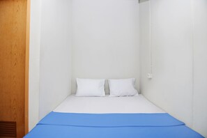 A small, single-bed room with white walls and a wooden door.