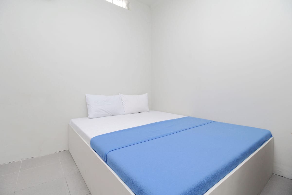 Habitación pequeña con una cama individual, blanca, y edredón azul y almohadas blancas.