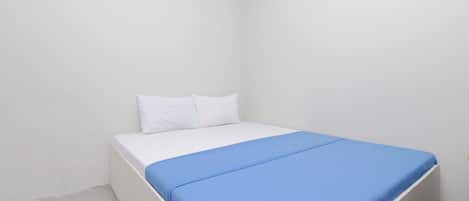 A small, white, single-bed room with a blue bedspread and white pillows.