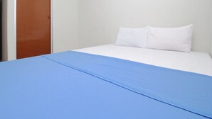 Una habitación con una cama, una puerta marrón y una pared blanca.