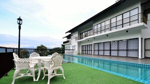Un edificio moderno con piscina, mobiliario exterior y vistas a la montaña.