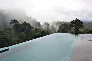 Vista despejada de una piscina con borde de azulejos, rodeada de exuberante vegetación y montañas brumosas al fondo.