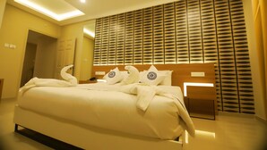 A hotel room with a bed, a headboard, a wall with a geometric pattern, and a ceiling light. - Noorjehans Grand Noor (Palakkad)