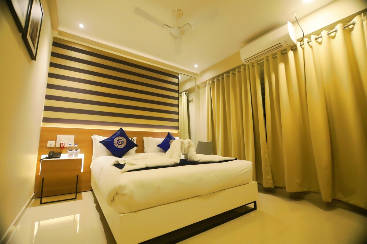 Une chambre d’hôtel avec un lit, une table de chevet, une commode, un ventilateur de plafond et une fenêtre avec des rideaux.