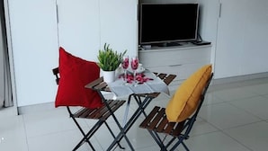 Un pequeño comedor con una mesa dispuesta para dos personas, una planta en maceta y un televisor de pantalla plana montado en la pared.