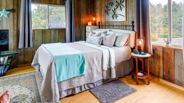 Quarto com painéis de madeira, cama, mesa de cabeceira e janela com cortinas.
