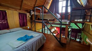 Una baita di legno con un letto a castello, un letto singolo e una scala che conduce a un piano superiore.