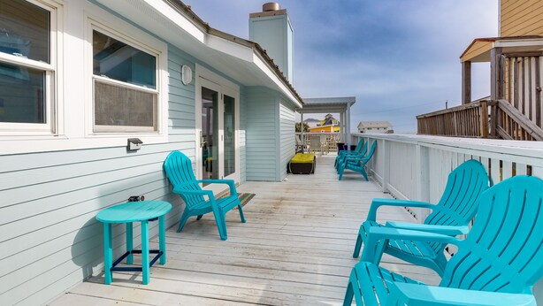 Een houten terras met turquoise Adirondack-stoelen en een kleine tafel, met uitzicht op een strand.