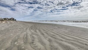 Een zandstrand met voetafdrukken en een verre kustlijn met gebouwen.