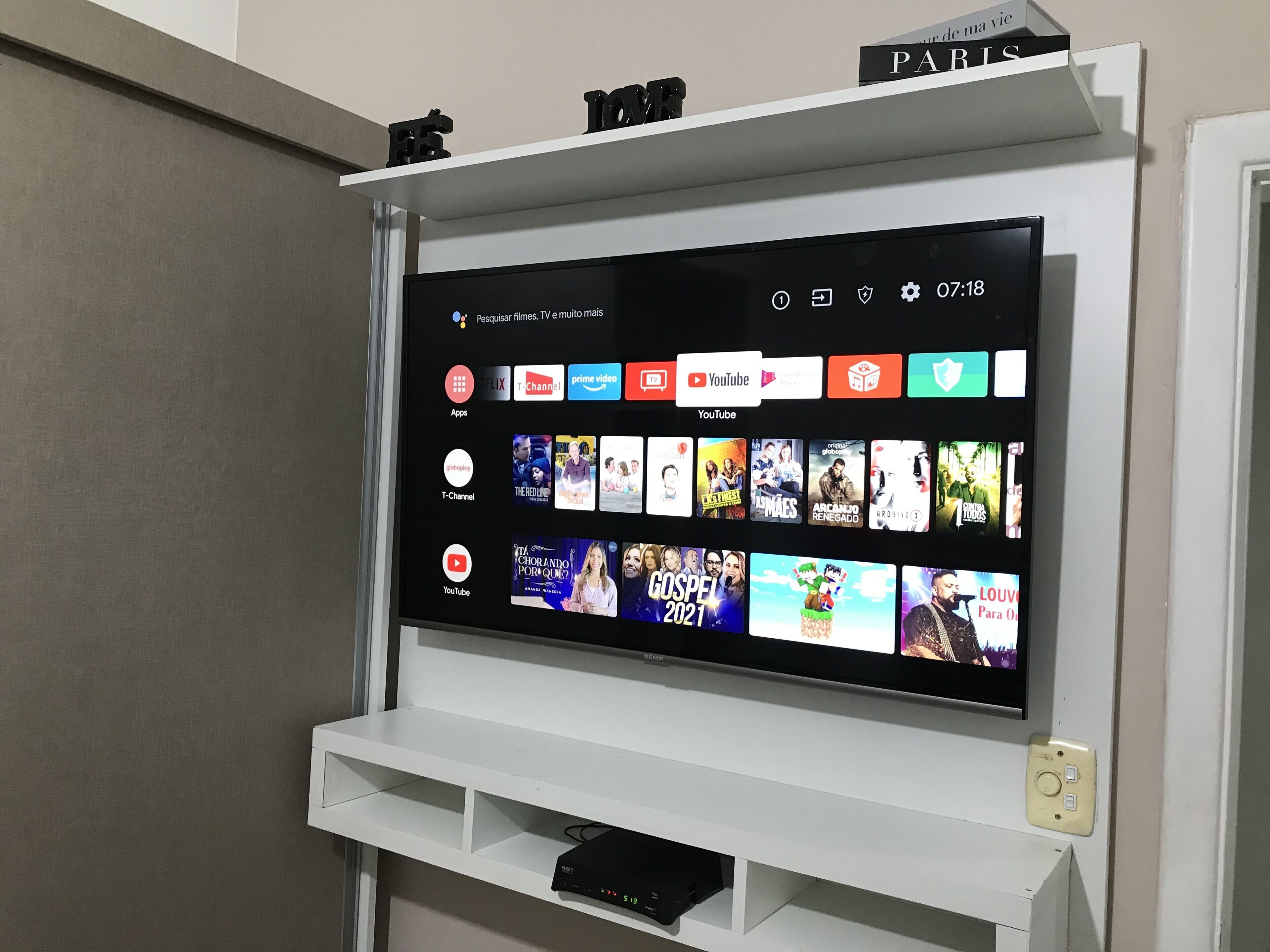 Un televisor de pantalla plana montado en una pared blanca con un estante encima.