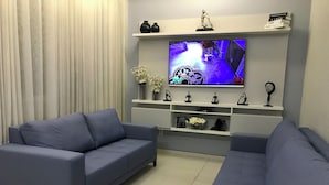 Una sala moderna con un sofá gris, un televisor de pantalla plana montado en la pared y objetos decorativos en estanterías.
