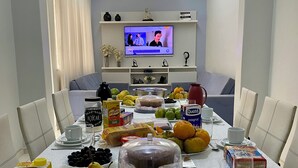 A dining table set with various fruits, nuts, and beverages, with a television in the background. - Apartment in Copacabana, 4 bedrooms, 3 bathrooms, 50 meters from the beach, shops, and supermarket. (Rio de Janeiro)